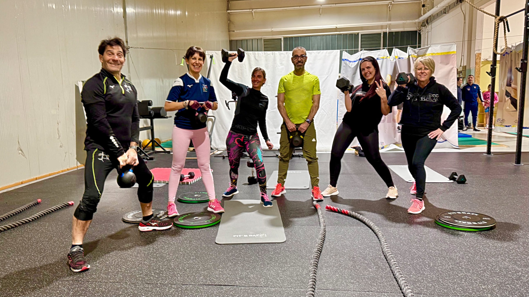 Sei persone si allenano con kettlebell e funi nella sala di preparazione atletica