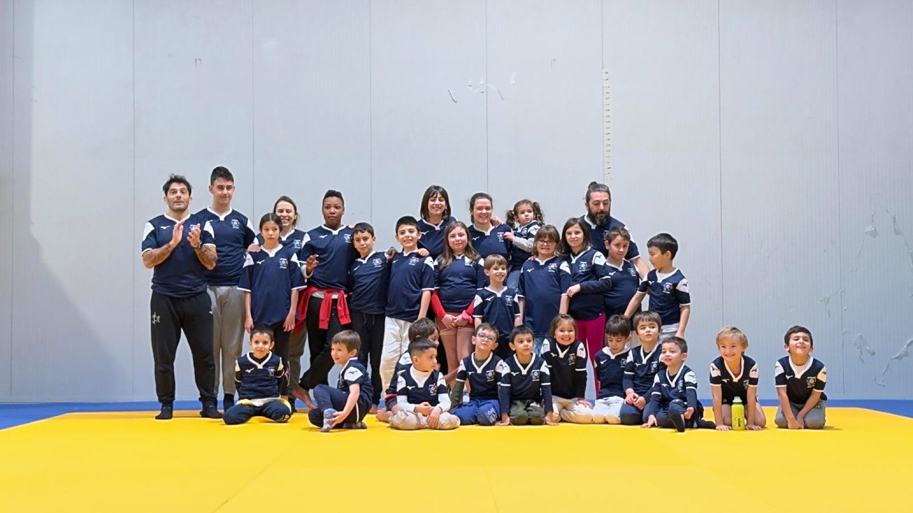 I bambini e le bambine del gruppo in posa sul tatami giallo con gli istruttori