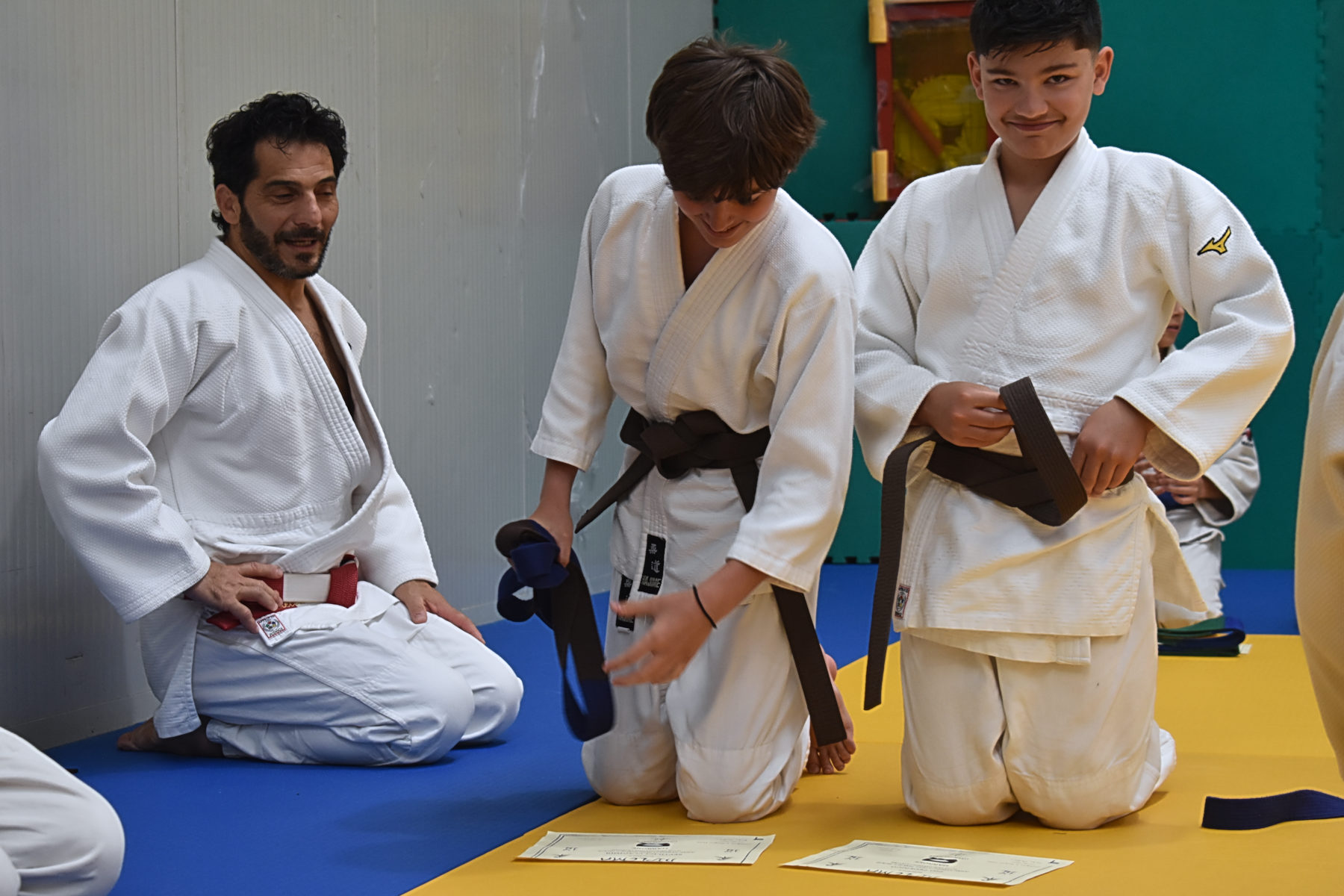 Un istruttore e due ragazzi in judogi, in ginocchio e in piedi sul tatami