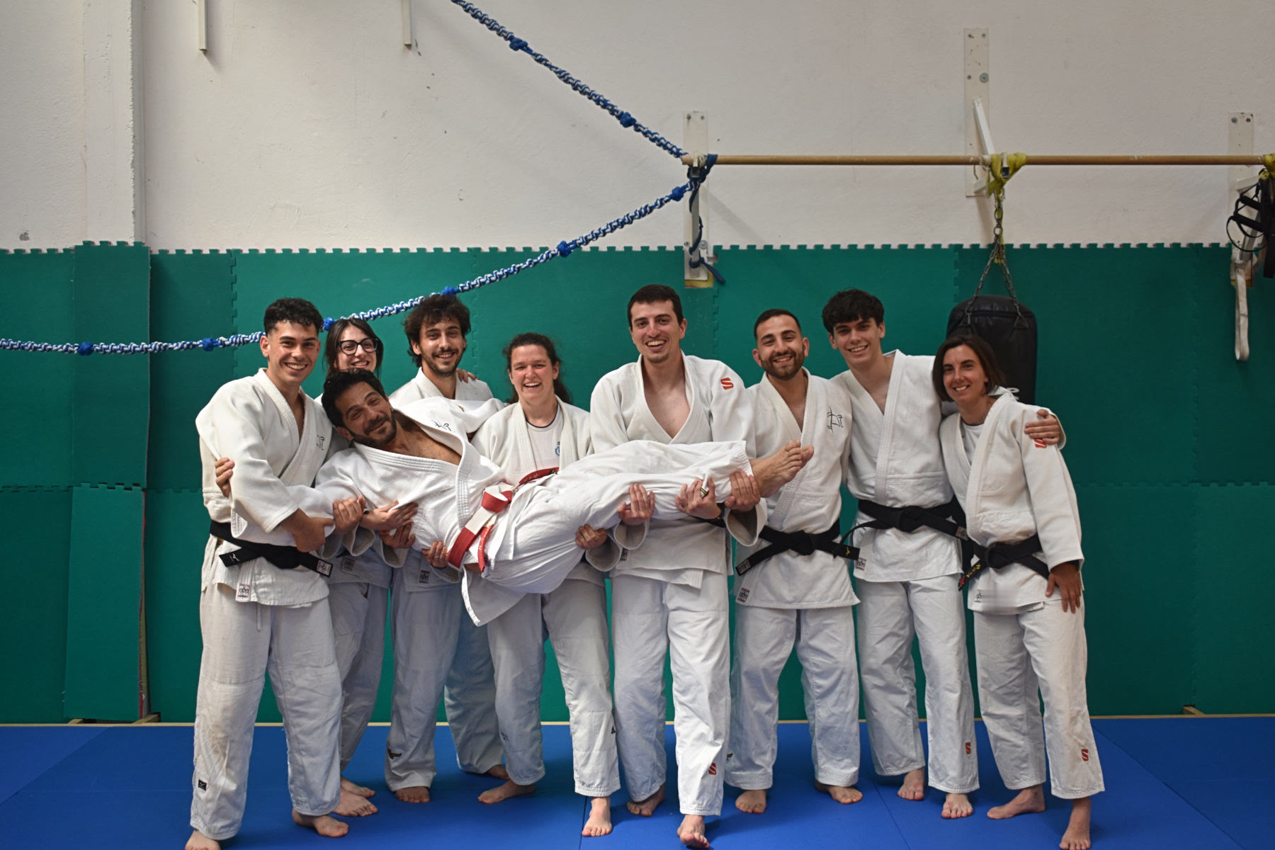 Un gruppo di judoka ride mentre solleva un compagno nella palestra